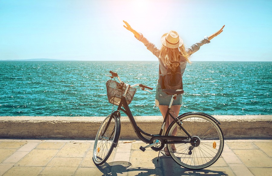 Blonde woman in summer hat with her bicycle walking coastline by the sea beach. Sea view. Freedom. W